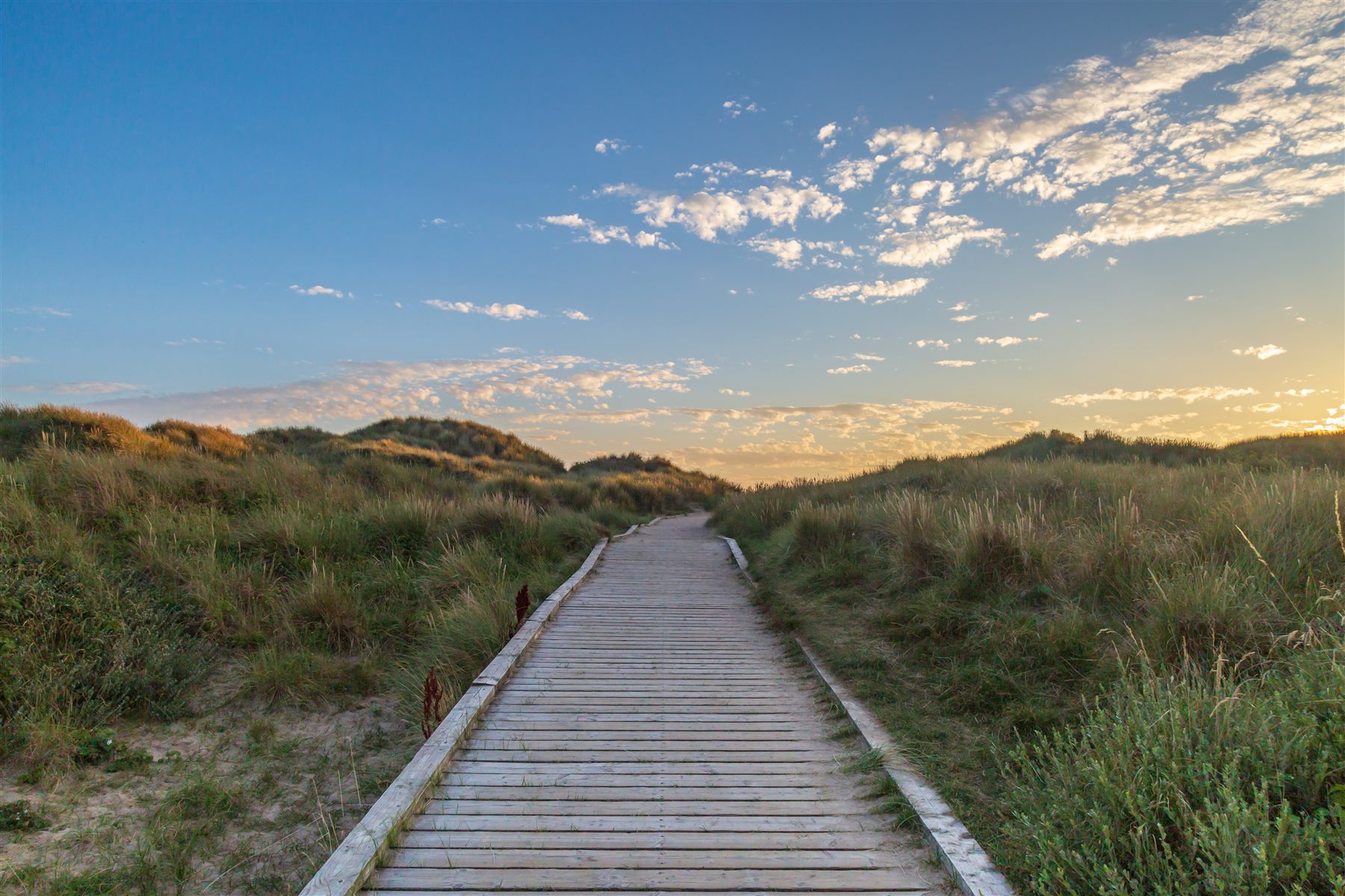 A wooden pathway leading toward the sea at sunset